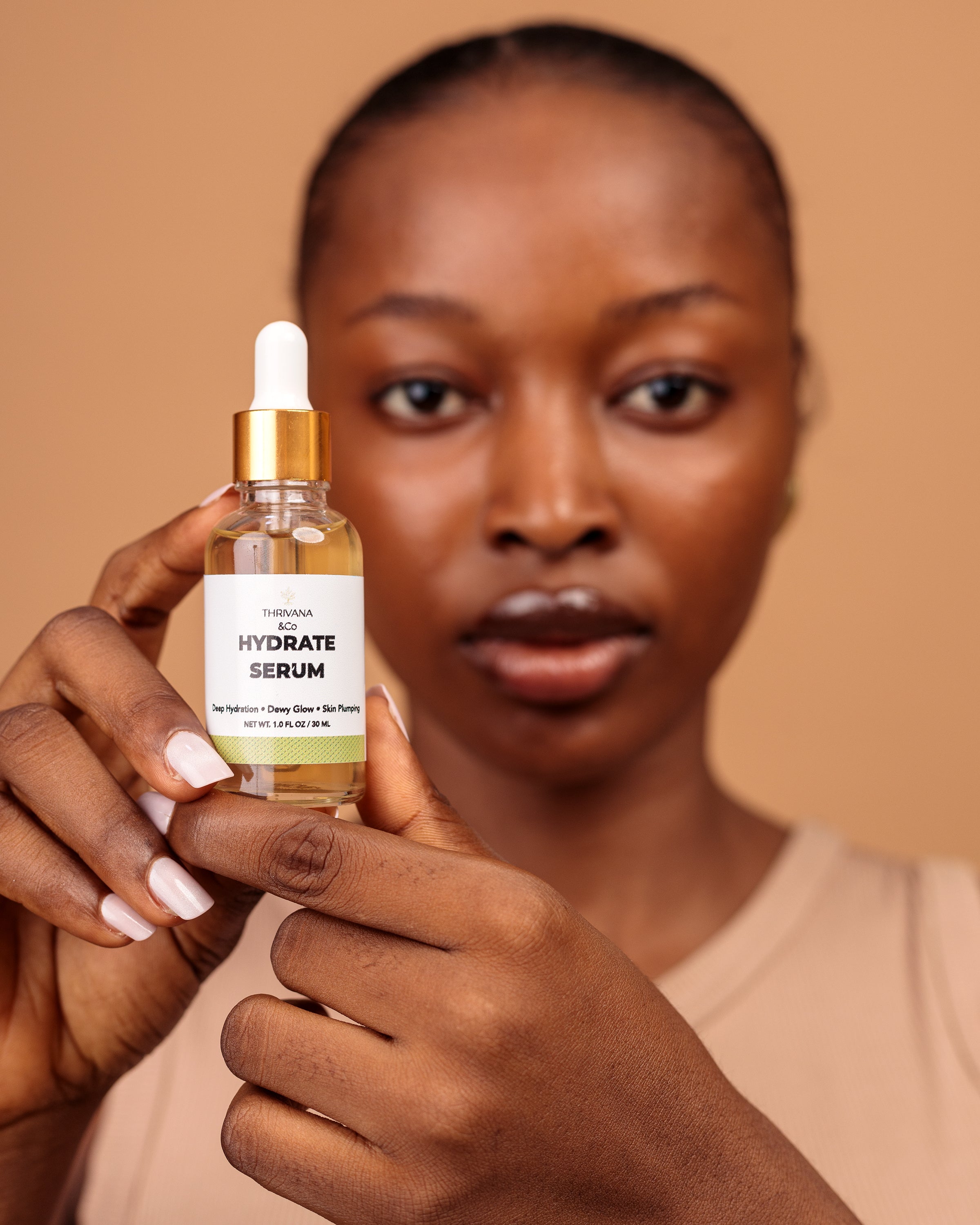 Woman holding a bottle of 'Hydrate Serum' against a beige background