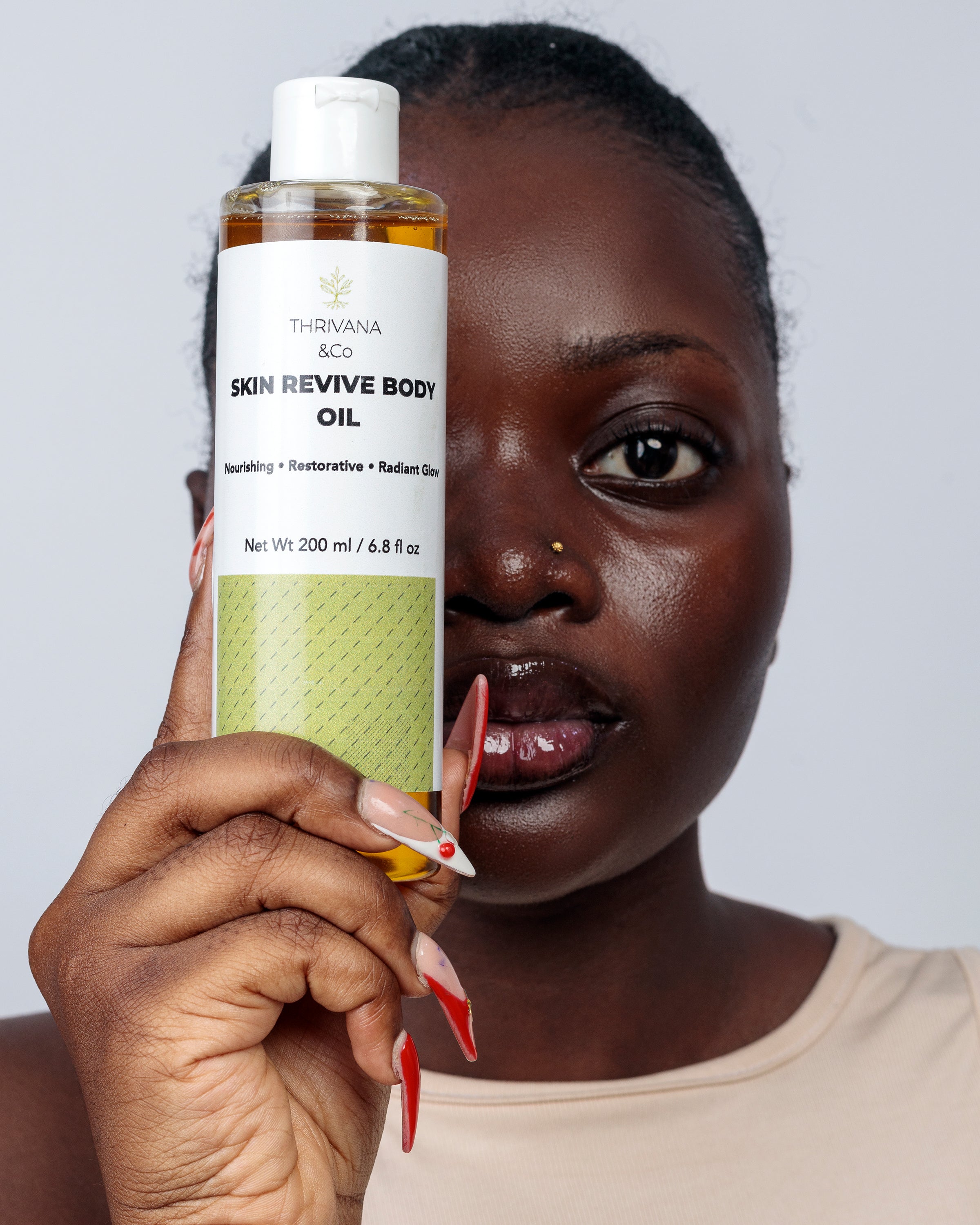 Woman holding a bottle of Thrivana & Co. Skin Revive Body Oil against a plain background