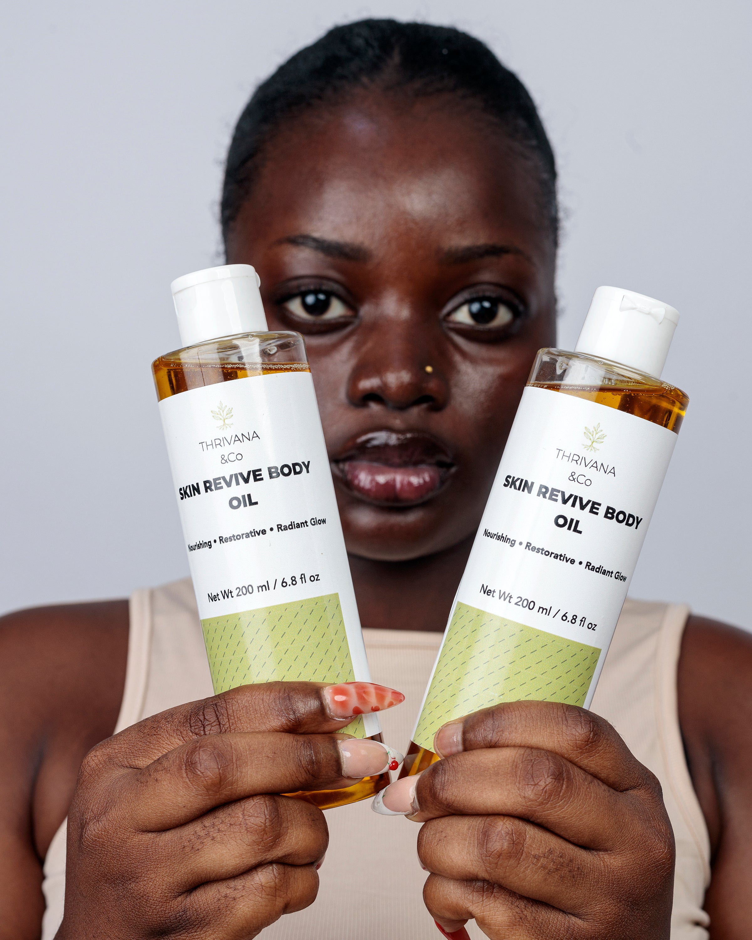 Woman holding two bottles of Skin Revive Body Oil against a plain background